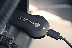A Chromecast stick plugged into the HDMI port of a TV. The cable attached to the other end is the USB power supply.