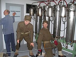 Two saboteurs and a facility employee shown adjacent to the electrolysis chambers