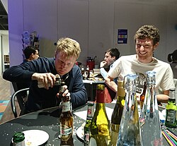 A person paying close visual attention to their use of a bottle opener, ignoring the other people around them