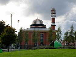 A mosque viewed from across a green. The mosque is fairly cubic with a central dome and a spire-like dome on one edge.