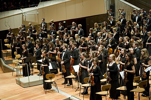 Members of a youth orchestra standing to acknowledge applause after performing.