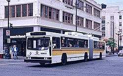 An articulated trolleybus on a city street, connected to overhead wires suspended from poles in the background