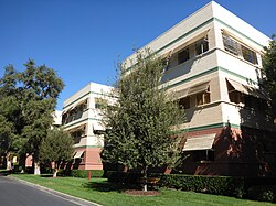 Three story building with green stripes surrounded by some trees