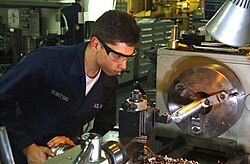 A fireman turning a bar of metal on a lathe on the USS Harry S. Truman in 2004