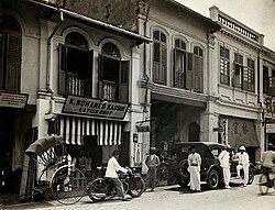 An arcade of shophouses with a road sweeper at work in the street of Kuala Lumpur, c. 1915–1925.