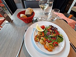 Plate of cooked scallops with a mixed salad, served with bread and wine in a French restaurant.