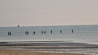 Fishers standing far from shore in shallow water while hauling a communal net.