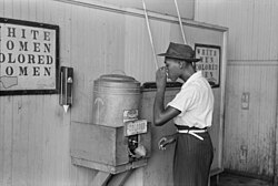 An African American man drinking at a "colored" drinking fountain in a streetcar terminal in Oklahoma City, Oklahoma, 1939