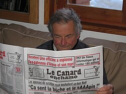 A reader consulting a copy of the newspaper Le Canard enchaîné.