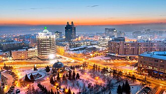 View of the part of Student Brigades Square and the intersection of Oktyabrskaya Highway, Serebrennikovskaya Street and Oktyabrskaya Street, as seen in 2017. In the lower left-hand corner, the part of the building of the Novosibirsk Globus Theatre is visible. In the center of the picture is the building at 50 Kommunisticheskaya Street, popularly known as "Batman" and "Plug".[30]