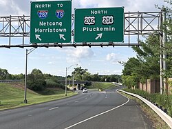 A multilane highway in a suburban area at a split, with two green signs over the road. The sign on the left reads north Interstate 287 to Interstate 78 Netcong Morristown with an arrow pointing to the upper right and the sign on the right reading north U.S. Route 202/U.S. Route 206 Pluckemin.