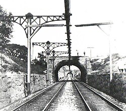 B&O's overhead third-rail system at Guilford Avenue in Baltimore, 1901, part of the Baltimore Belt Line. The central position of the overhead conductors was dictated by the many tunnels on the line: the ∩-shaped rails were located at the highest point in the roof to give the most clearance.[9]