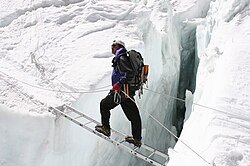 A mountain guide crossing a wide crevasse with a ladder bridge