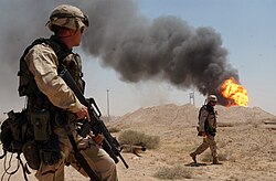 A US Army soldier watching a burning oil well at Rumaila oil field in April 2003; the fire was later extinguished by coalition personnel