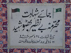 Plaque marking the location of the assassination of Benazir Bhutto, written in Urdu. Translation: Place of Martyrdom, Ms. Benazir Bhutto martyred. Benazir Bhutto was killed by a suicide terrorist in 2007.[b]