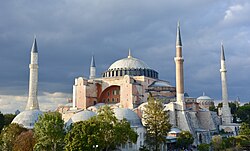 A reddish building topped by a large dome and surrounded by smaller domes and four towers