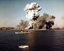 U.S. Navy and U.S. Army explosives teams destroy facilities and abandoned United Nations supplies in Hŭngnam on 24 December 1950, the last day of the amphibious evacuation of U.N. forces from Hŭngnam during the Korean War. The U.S. Navy high-speed transport USS Begor (APD-127) stands by in the foreground.