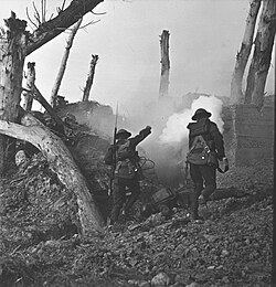 Two United States soldiers run toward a bunker past the bodies of two German soldiers.