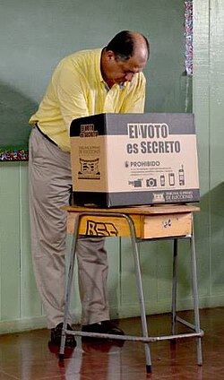 Presidential candidate Luis Guillermo Solís votes in the 2014 Costa Rican general election behind a privacy screen which says "The VOTE is SECRET"; Solís was elected president in the election
