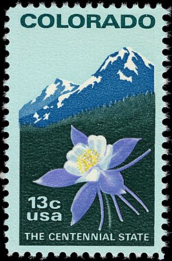 A postage stamp with a perforated edge with the text "COLORADO" at the top and two snow covered mountains. Below is a columbine flower with the text "13¢ USA" next to it and the motto "The Centennial State" across the bottom.