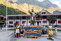 Welcome sign with statues of Inca figures in front of a building, with mountains in the background.