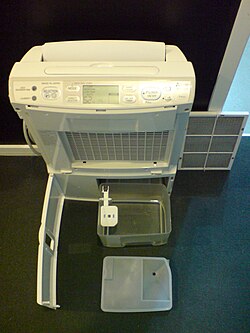 Partially disassembled portable dehumidifier (a Mitsubishi Electric Oasis), with condensate bucket and white-colored float sensor visible at center