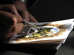An artist painting on thick watercolor paper