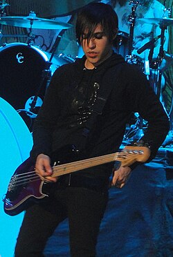 Pete Wentz of Fall Out Boy displaying features of emo fashion: skinny jeans, eye liner, and flat, straight, jet-black hair with long bangs covering the face