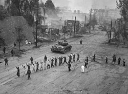 American M26 Pershing tanks in downtown Seoul, in the foreground, United Nations troops round up North Korean prisoners-of-war.