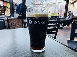 A pint glass partially filled with Guinness 0 poured from a can.