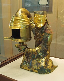 A gilded bronze oil lamp in the shape of a kneeling female servant, dated to the 2nd century BC, found in the tomb of Dou Wan, wife of Liu Sheng, Prince of Zhongshan; its sliding shutter allows for adjustments in the direction and brightness in light while it also traps smoke within the body.[73][358]