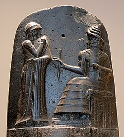 Hammurabi (standing), depicted as receiving his royal insignia from Shamash (or possibly Marduk). Hammurabi holds his hands over his mouth as a sign of prayer[8] (relief on the upper part of the stele of Hammurabi's code of laws).