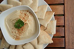 Hummus served in a bowl on a platter of pita bread