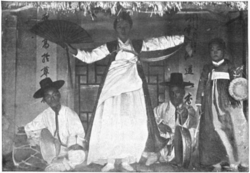 A person standing holding a paper fan with other people to the left and right