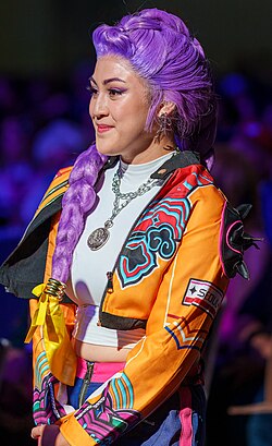 Waist-up photo of a cosplayer with a purple braided wig, dressed in Rumi's yellow jacket
