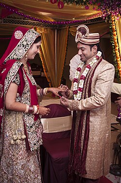 A man as the groom and a woman as the bride in a Hindu North Indian wedding, the groom wearing a sherwani and pagri turban and the bride wearing a sari.