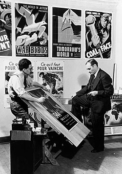John Grierson (right), National Film Board (NFB) Commissioner, and Harry Mayerovitch, director of the Wartime Information Board's (WIB) Graphic Arts Division, examine posters in 1944.