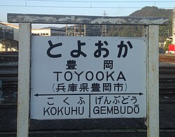 Former Japan National Railways–style board of Toyooka Station. For the two adjacent stations, "GEMBUDŌ" follows the Hepburn romanization system, but "KOKUHU" follows both the Nihon-shiki and Kunrei-shiki systems.